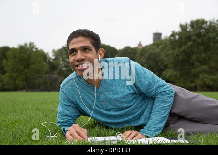 Giovane uomo disteso sull'erba facendo i compiti di scuola Foto Stock