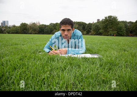 Giovane uomo disteso sull'erba facendo i compiti di scuola Foto Stock