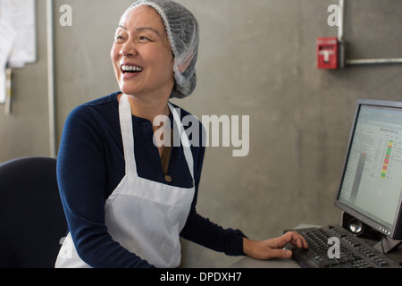 Donna che indossa il grembiule e retina per capelli utilizzando il computer Foto Stock