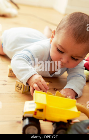 Il bambino che giace sulla parte anteriore a giocare con blocchi e carrello Foto Stock