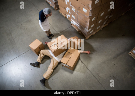 Donna che guarda l'uomo sdraiato sul pavimento coperto da scatole di cartone in magazzino Foto Stock