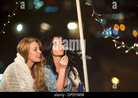 Due amiche a soffiare bolle in parte sul tetto Foto Stock