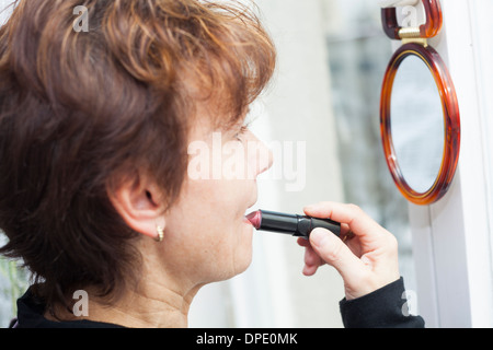 Donna di mezza età il rossetto e guardando a specchio. Foto Stock