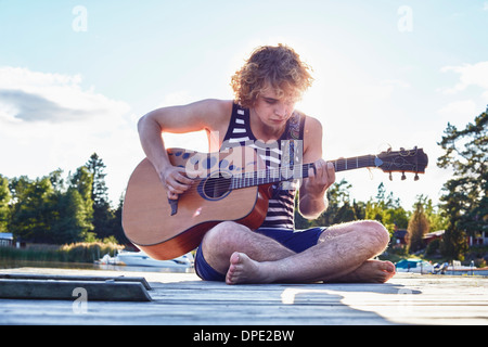 Giovane uomo a suonare la chitarra sul molo, Gavle, Svezia Foto Stock