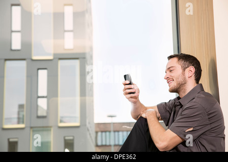 Imprenditore seduto sul davanzale utilizza lo smartphone Foto Stock