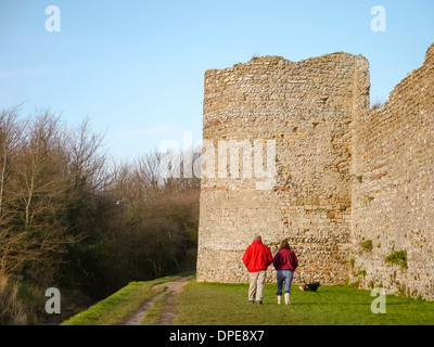 Un adulto giovane a piedi il loro cane intorno al muro perimetrale di Portchester Castle in Hampshire, Inghilterra, su una chiara inverni di giorno. Foto Stock