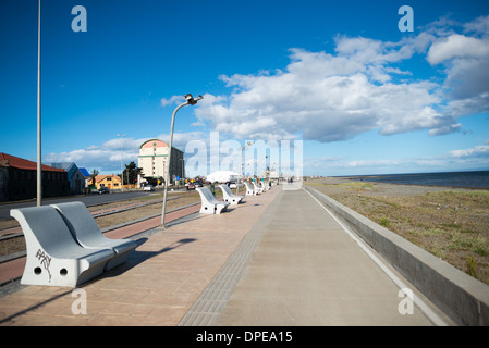 Costanera del Estrecho Benches Promenade Punta Arenas Cile / PUNTA ARENAS, Cile - panche di cemento pesante fiancheggiano la Costanera del Estrecho, una passeggiata pavimentata parallela allo stretto di Magellano. Fondata nel 1848, la città si è sviluppata lungo questo litorale come un porto di rifornimento critico per le spedizioni globali. La via navigabile visibile appena oltre il percorso fungeva da rotta principale navigabile tra l'Oceano Atlantico e l'Oceano Pacifico fino a quando il Canale di Panama dirottava il traffico marittimo. Foto Stock