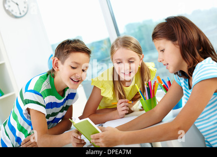 Compagni di classe essendo curiosi di sapere che cosa il loro amico la lettura Foto Stock