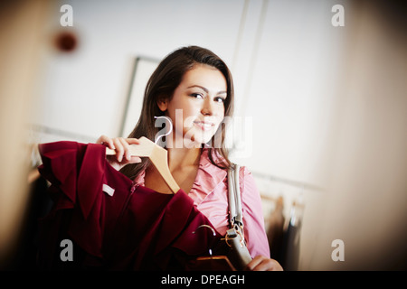 Giovane donna cercando top rosa su appendiabiti Foto Stock