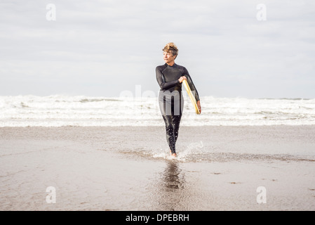 Femmina matura bodyboarder pagaiando sulla costa del Devon, Regno Unito Foto Stock