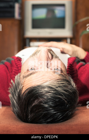 Primo piano della senior uomo disteso nella parte anteriore della TV e guardando in alto Foto Stock