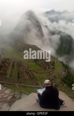 26 nov 2006 - Machu Picchu, Perù - con la nebbia mattutina non ancora sollevato, un 'gringo' (straniero) recensioni la sua mappa del Inkan rovine di Machu Picchu seduto su una mensola che si affaccia su tutto il sito. Machu Picchu è stato costruito nel corso di centinaia di anni da parte dei lavoratori sotto il controllo dell'elite Incans, che alla fine sono stati massacrati dai colonialists spagnoli in cerca di oro. (Credito mi Foto Stock