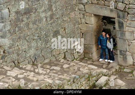 26 nov 2006 - Machu Picchu, Perù - Dopo aver impostato il tempo di rilascio dell'otturatore fotocamera su un treppiede, un Giapponese giovane posano per una foto in una porta di rovine Inca di Machu Picchu. Il sito antico è il più noto simbolo dell'impero Inca che ricopriva gran parte del Sud America. Più di 400.000 persone hanno visitato "La Città perduta degli Incas" nel 2000. (Credito Immagine: © Zack Baddorf/ZUMA Foto Stock