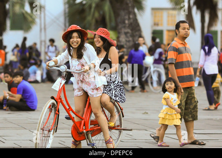 Due giovani donne indonesiane godendo di una corsa in bicicletta in Piazza Fatahillah in Jakarta Kota (città vecchia), Indonesia Foto Stock