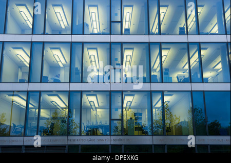 Facciata di un ufficio moderno edificio con luci accese in uffici di sera, Monaco di Baviera, Germania Foto Stock