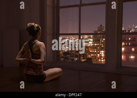 La donna a praticare yoga per finestra Foto Stock