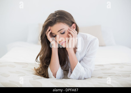 Triste marrone casual donna dai capelli in bianco pigiama sdraiato sul suo letto Foto Stock