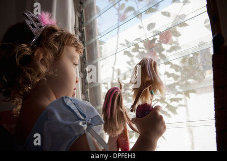 Toddler femmina guardando fuori della finestra tenendo premuto fino bambole Foto Stock