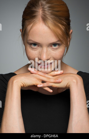 Giovane donna mento di appoggio sulle mani, sorridente, ritratto Foto Stock