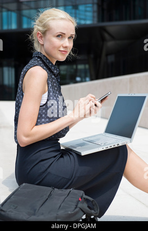 Imprenditrice utilizzando computer portatile e lo smartphone per lavorare in esterno Foto Stock