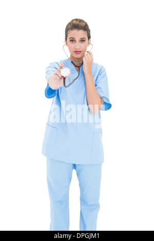 Stern brown pelose infermiere in blu scrubs utilizzando uno stetoscopio Foto Stock