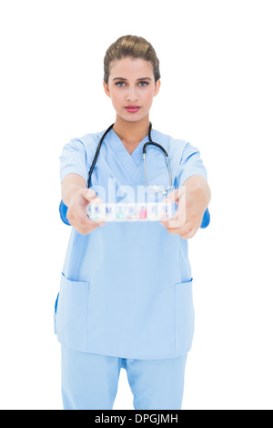 Stern brown pelose infermiere in scrub blu che mostra una scatola di farmaci Foto Stock