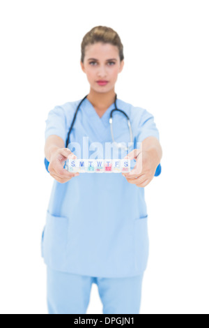 Gravi dai capelli marroni infermiere in scrub blu che mostra una scatola di farmaci Foto Stock