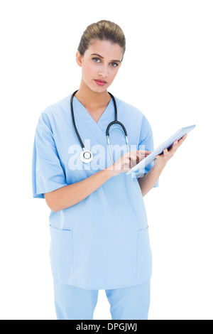 Stern brown pelose infermiere in blu scrubs utilizzando un tablet pc Foto Stock