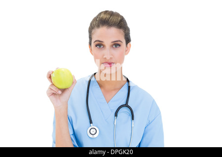 Gravi dai capelli marroni infermiere in blu scrubs tenendo una mela verde Foto Stock