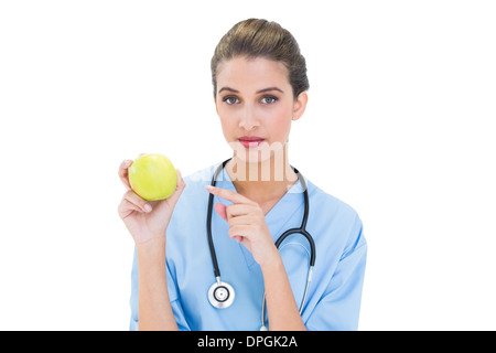 Stern brown pelose infermiere in blu scrubs puntando un Apple con il suo dito Foto Stock