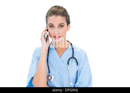 Stern brown pelose infermiere in blu scrubs effettuando una chiamata telefonica Foto Stock