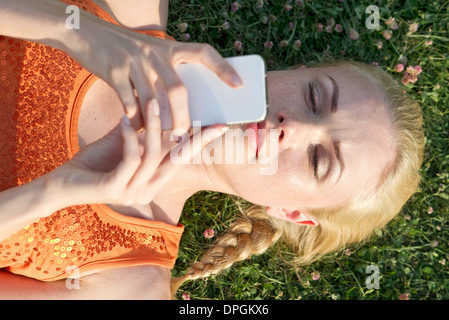 Giovane donna sdraiata su erba utilizza lo smartphone Foto Stock