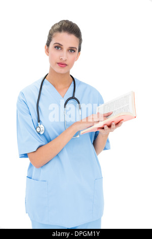 Gravi dai capelli marroni infermiere in scrub blu in possesso di un libro Foto Stock