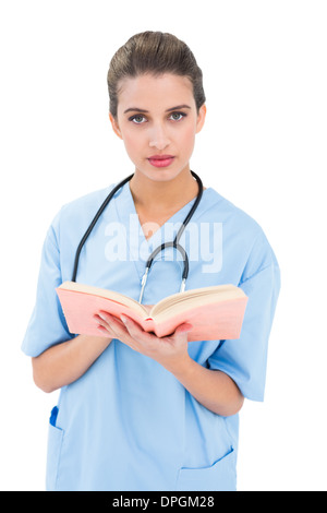 Stern brown pelose infermiere in scrub blu in possesso di un libro Foto Stock