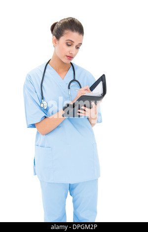Concentrato dai capelli marroni infermiere in blu scrubs il riempimento di un ordine del giorno Foto Stock