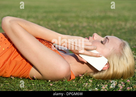 Giovane donna sdraiata su erba parlando sullo smartphone Foto Stock