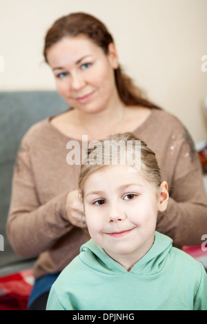 Da intreccio madre i capelli di sua figlia seduta in ambiente domestico Foto Stock