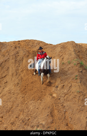 Un cowboy a cavallo di un quarter horse in cima a uno sperone, western hilltop contro un cielo azzurro. Foto Stock