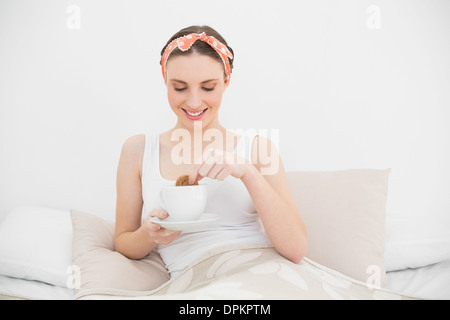 Donna sorridente immergendo un biscotto nel suo caffè Foto Stock