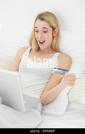 Felice sorpresa donna home shopping con il suo computer portatile sdraiato sul suo letto Foto Stock