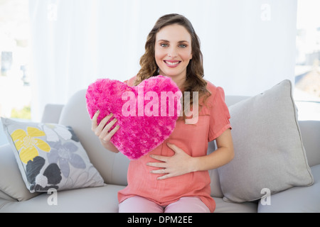 Contenuto donna incinta tenendo un cuscino seduta sul divano in soggiorno Foto Stock