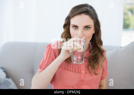 Splendida donna incinta di bere un bicchiere di acqua seduto in salotto Foto Stock