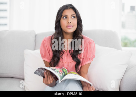 Considerato carino brunette seduta sul lettino holding magazine Foto Stock