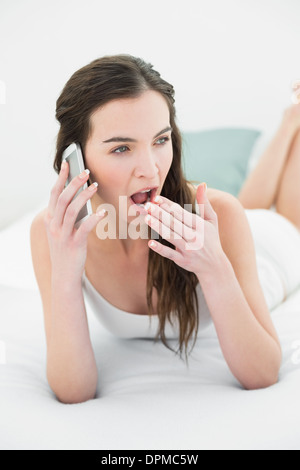 Assonnato donna sbadigliare mentre si utilizza il telefono cellulare a letto Foto Stock