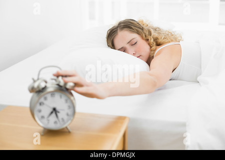 Piuttosto stanco bionda giacenti nel letto di spegnere la sveglia Foto Stock