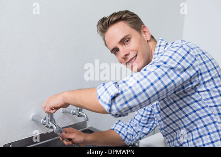 Plumber sorridente che fissa il rubinetto dell'acqua con le pinze Foto Stock