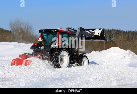 Il trattore spazza la neve su un cantiere in inverno. Foto Stock