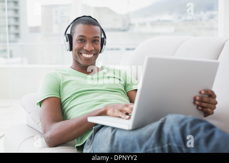 Ritratto di sorridere Afro Uomo con cuffie utilizzando computer portatile sul divano Foto Stock