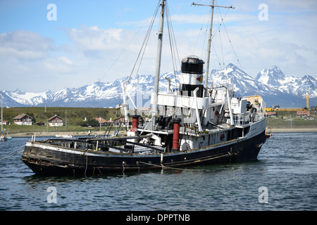 USHUAIA, Argentina - il relitto del Santo Cristoforo (HMS Justice) aggirato nel porto di Ushuaia, Argentina. Il Sain Christopher è un rimorchiatore di salvataggio costruito dagli americani che servì nella Royal Navy britannica nella seconda guerra mondiale Dopo la guerra fu smantellata dal Royal Nay e venduta per operazioni di salvataggio nel canale di Beagle. Dopo aver sofferto problemi motori nel 1954, fu saccheggiata nel 1957 nel porto di Ushuaia, dove ora funge da monumento ai naufragi della regione. Le montagne innevate in lontananza si trovano sul canale di Beagle in Cile. Situato sulla punta meridionale della SO Foto Stock