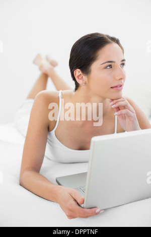 Premurosa donna informale con il computer portatile a letto Foto Stock